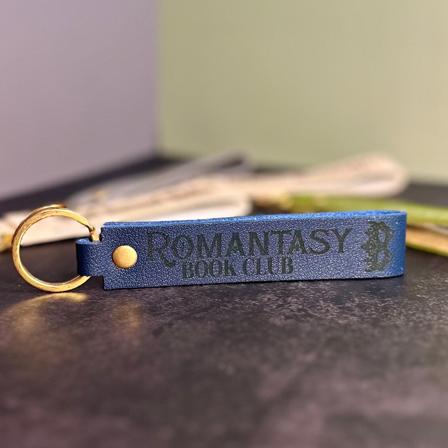 A navy blue faux-leather keychain with 'Romantasy book club' etched into it.