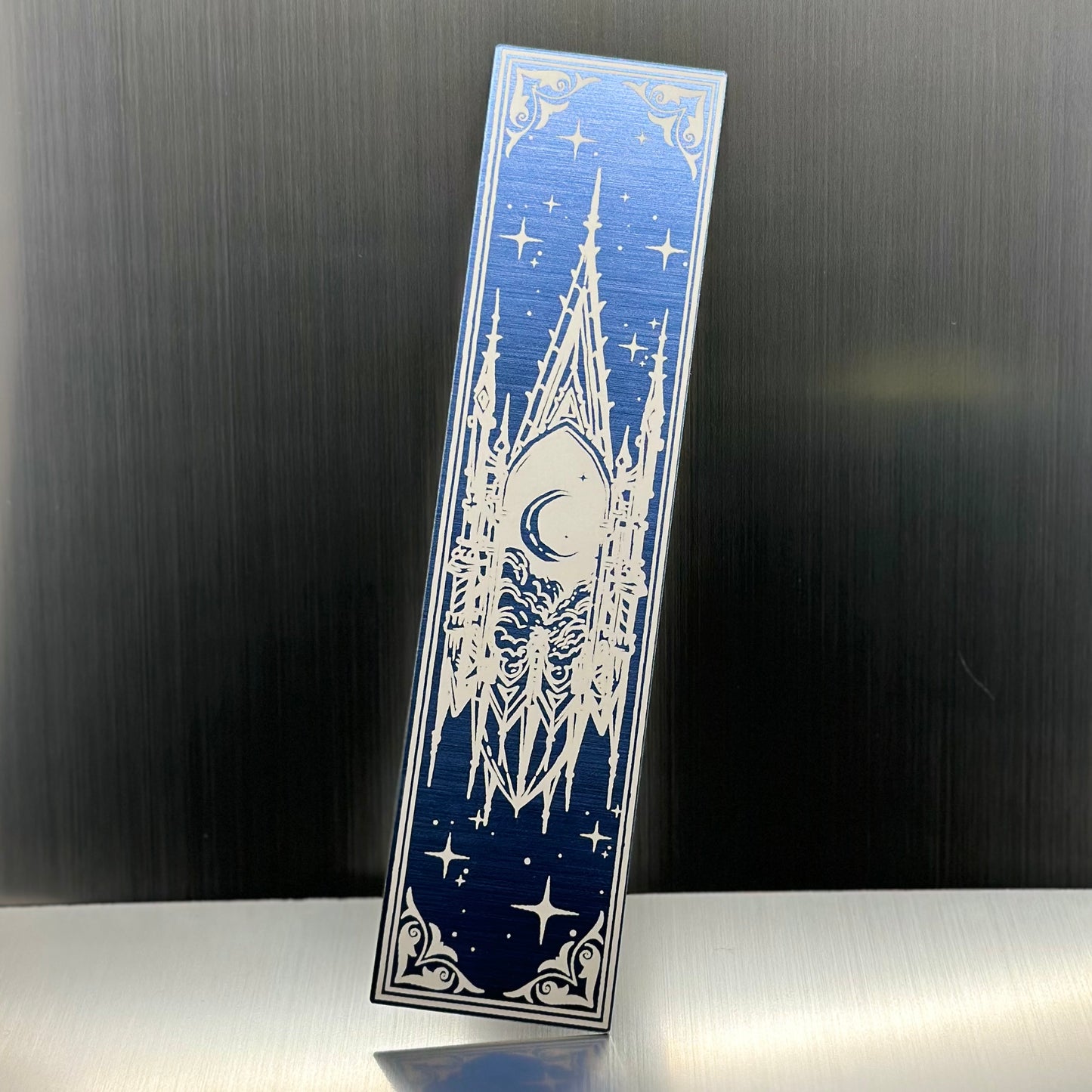 A blue metallic acrylic bookmark with a floating cathedral window showing clouds and a moon