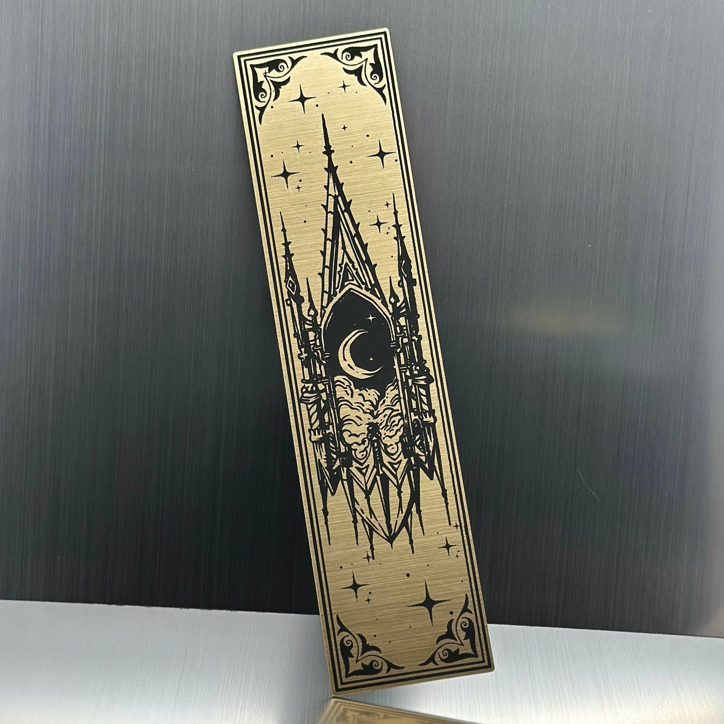 A gold metallic acrylic bookmark with a floating cathedral window showing clouds and a moon