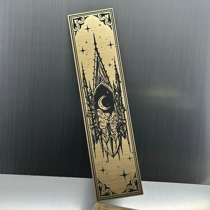 A gold metallic acrylic bookmark with a floating cathedral window showing clouds and a moon