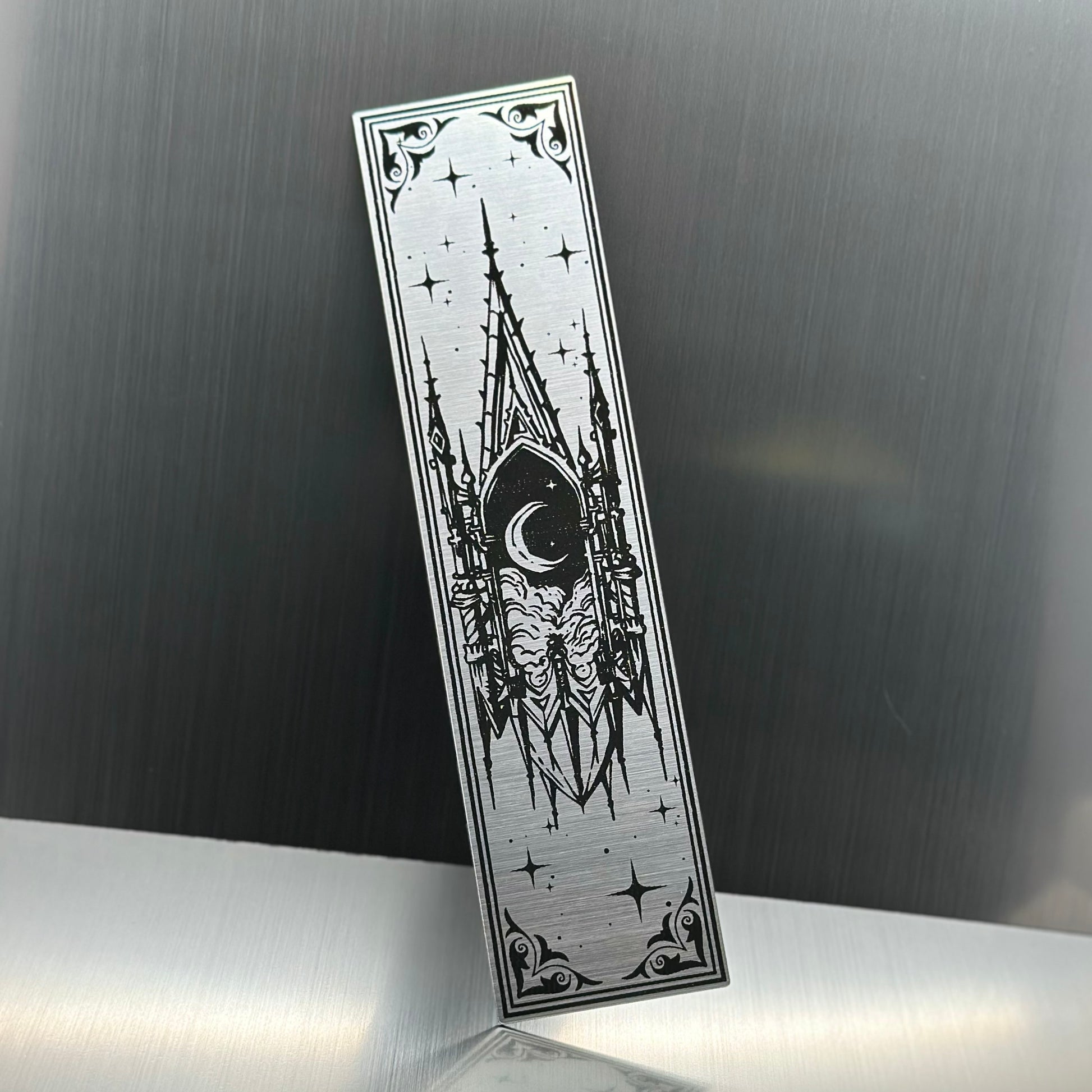 A silver metallic acrylic bookmark with a floating cathedral window showing clouds and a moon