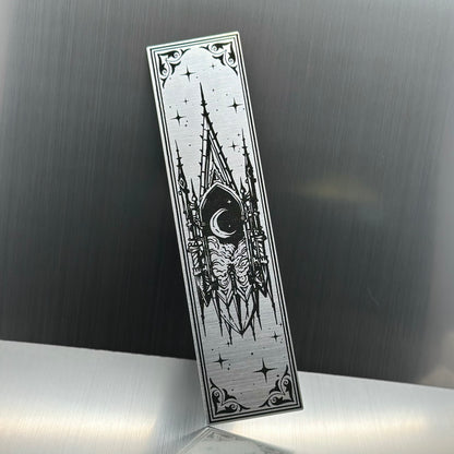 A silver metallic acrylic bookmark with a floating cathedral window showing clouds and a moon
