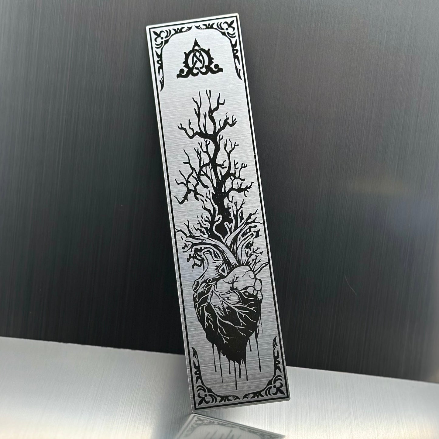A silver metallic acrylic bookmark with a heart with a tree growing out of it.