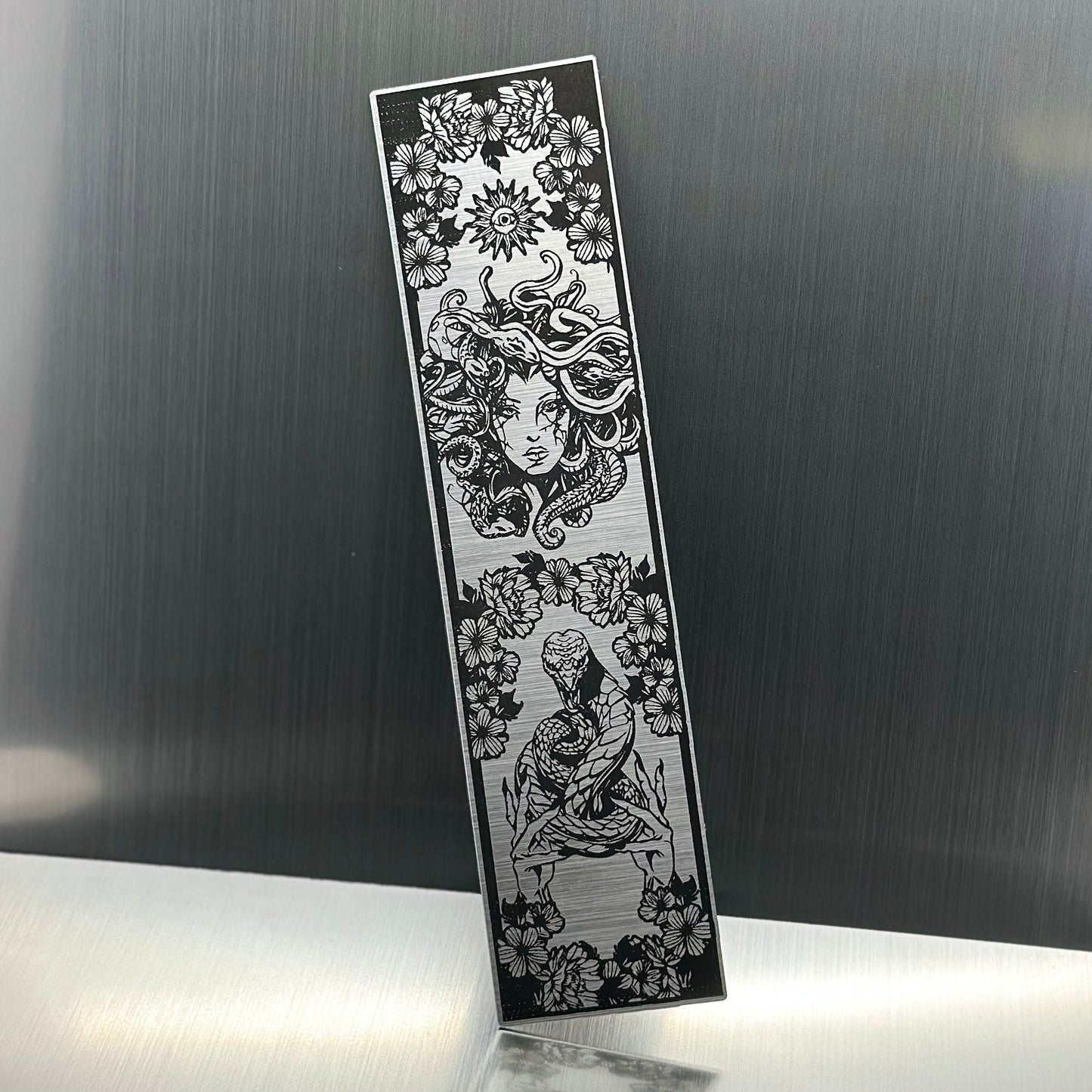 A silver metallic acrylic bookmark with Medusa's head at the top and a snake being held at the bottom
