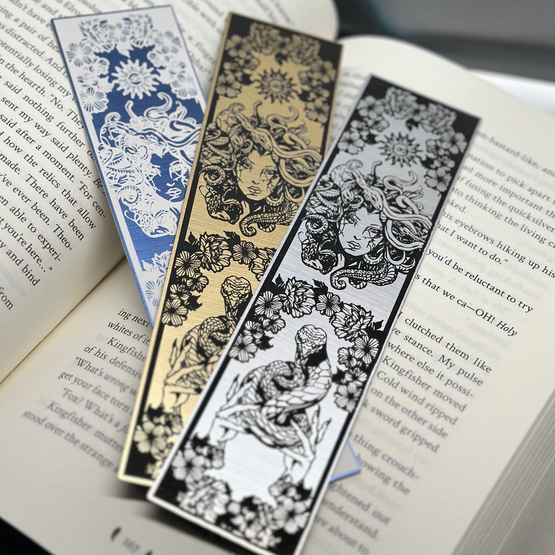 A trio of metallic bookmarks with Medusa's head at the top and a snake being held at the bottom on metallic acrylic.