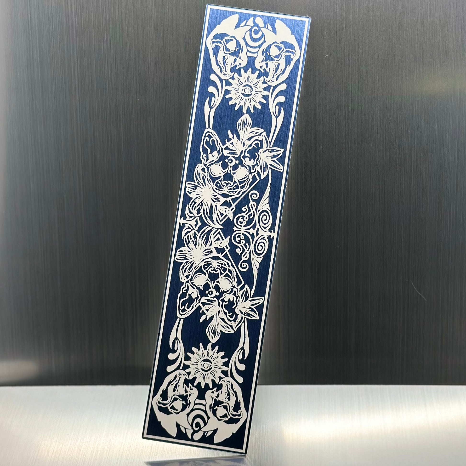 A blue metallic acryclic bookmark with cat skulls