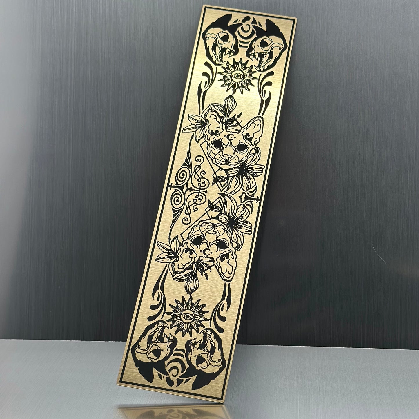 A gold metallic acryclic bookmark with cat skulls
