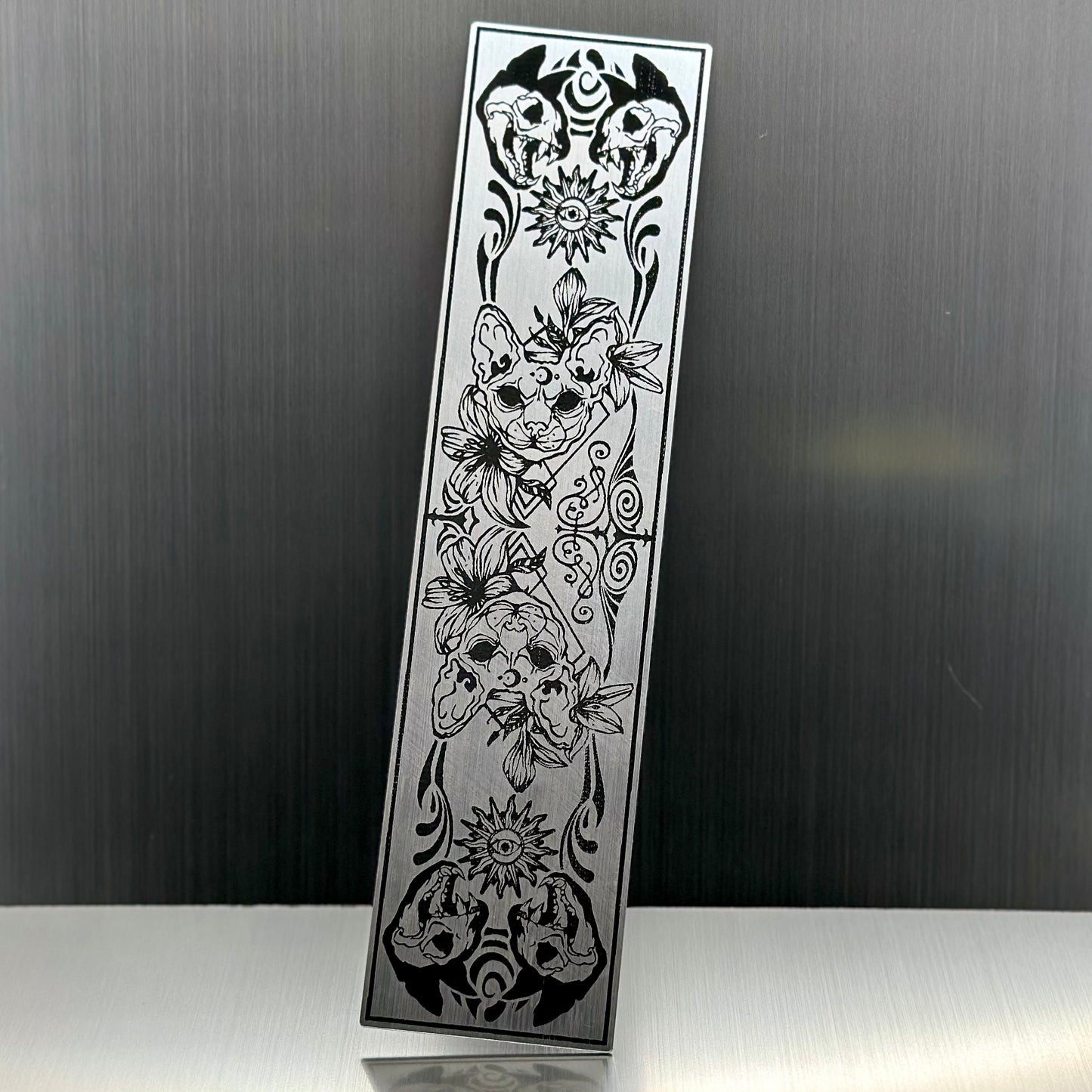 A silver metallic acryclic bookmark with cat skulls