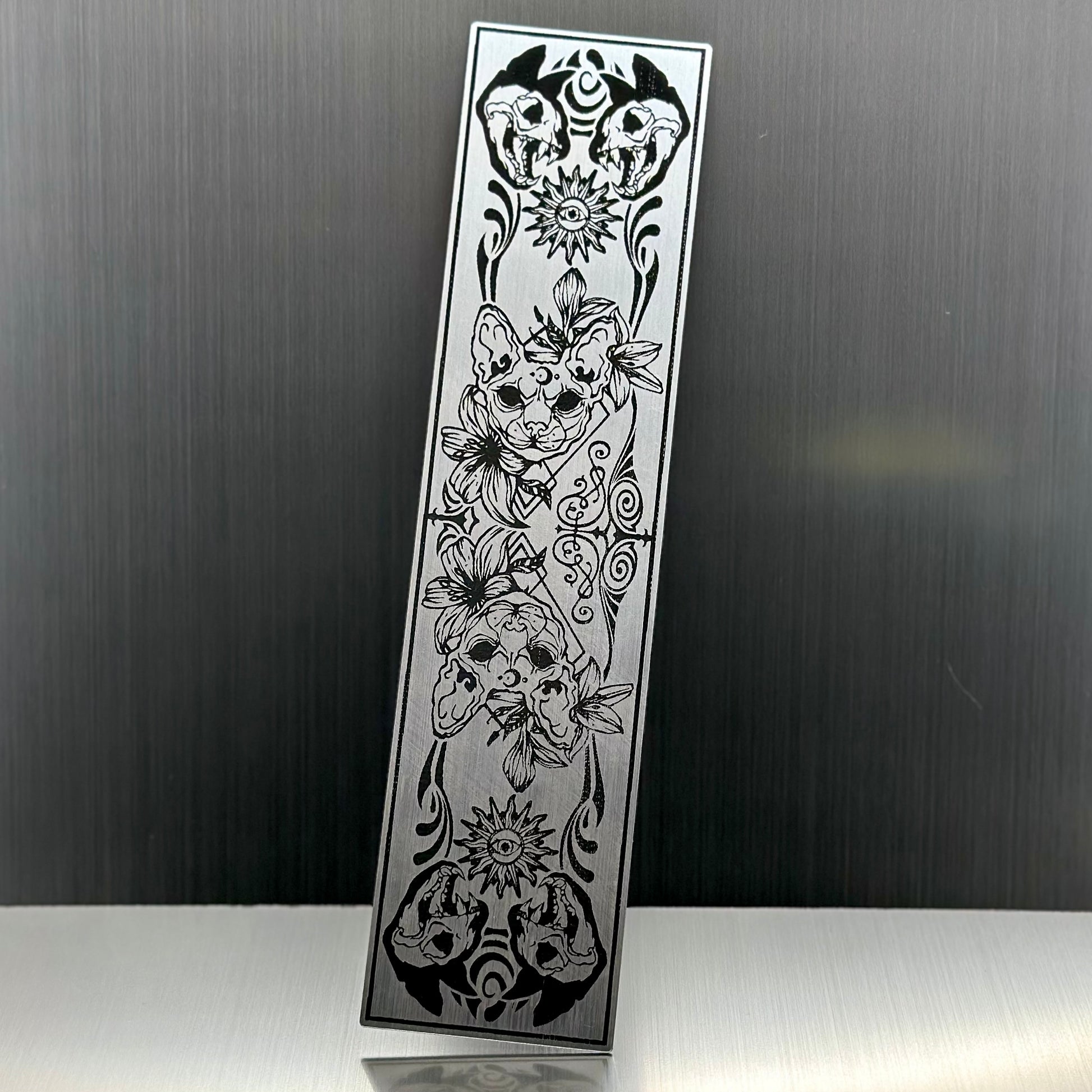 A silver metallic acryclic bookmark with cat skulls