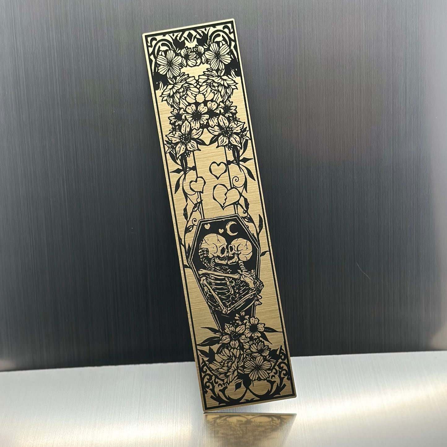 A gold metallic acrylic bookmark with skeletons embracing