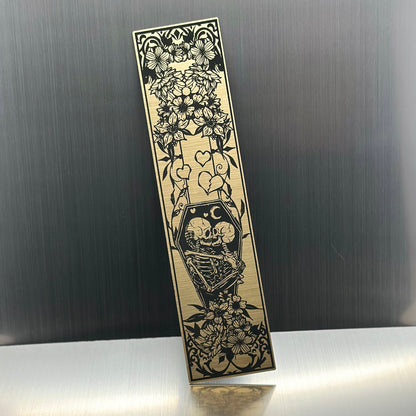 A gold metallic acrylic bookmark with skeletons embracing