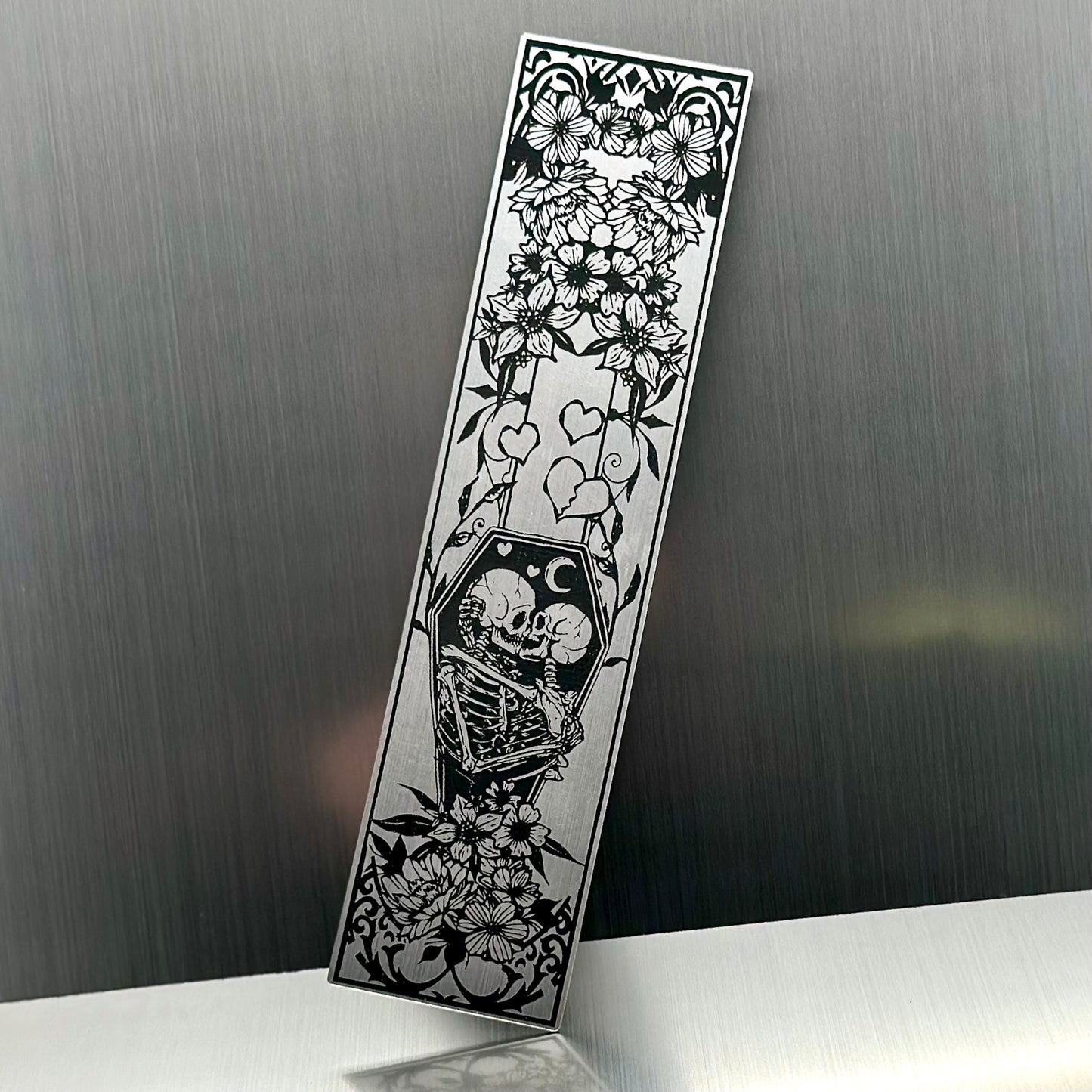 A silver metallic acrylic bookmark with skeletons embracing