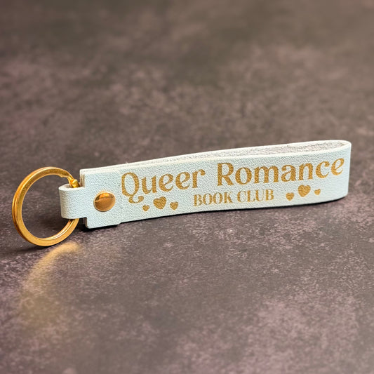 A sky blue faux-leather keychain with 'queer romance book club' etched into it.
