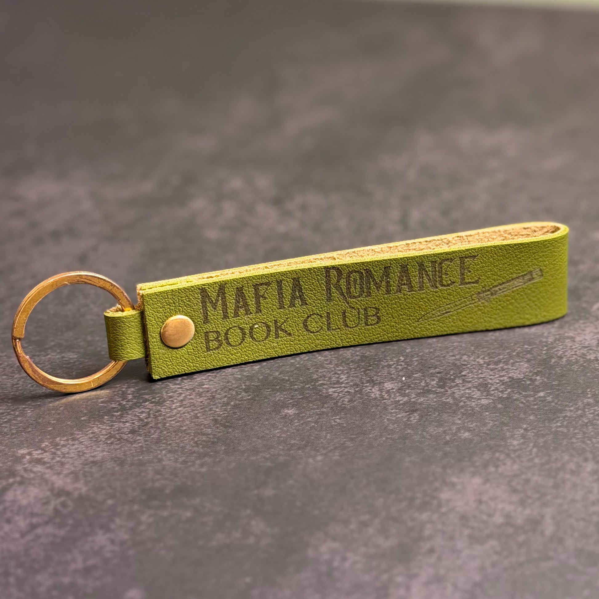 An olive green faux-leather keychain with 'Mafia romance book club' etched into it.