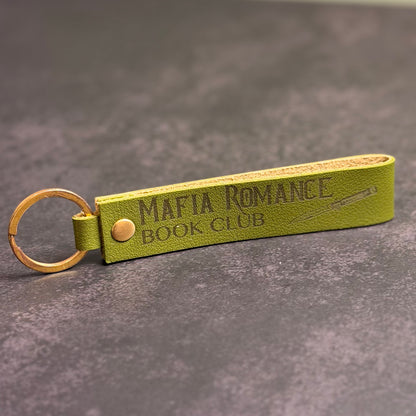 An olive green faux-leather keychain with 'Mafia romance book club' etched into it.