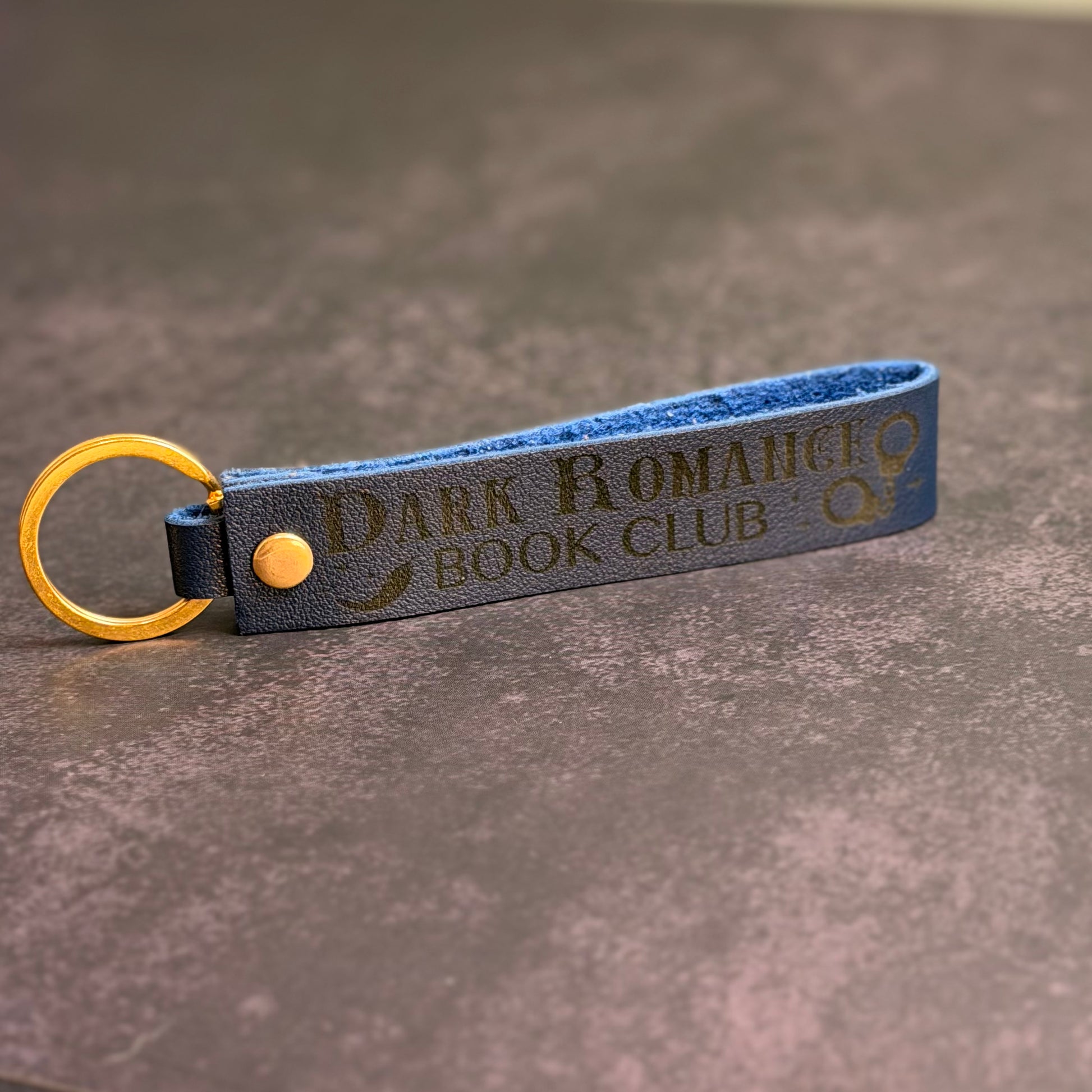 A navy blue faux-leather keychain with 'Dark Romance book club' etched into it.
