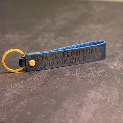 A navy blue faux-leather keychain with 'Dark Romance book club' etched into it.