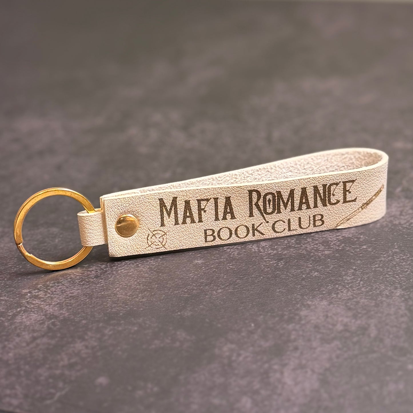 A beige faux-leather keychain with 'Mafia romance book club' etched into it.
