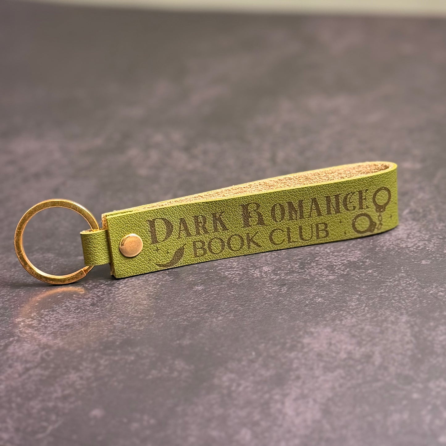 An olive green faux-leather keychain with 'Dark Romance book club' etched into it.