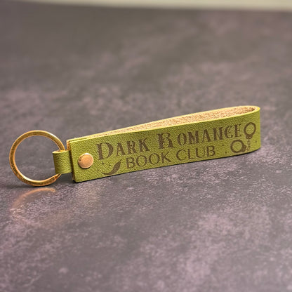 An olive green faux-leather keychain with 'Dark Romance book club' etched into it.