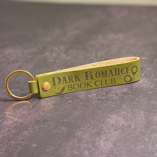 An olive green faux-leather keychain with 'Dark Romance book club' etched into it.