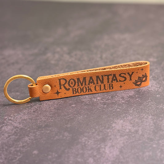 A brown faux-leather keychain with 'Romantasy book club' etched into it.