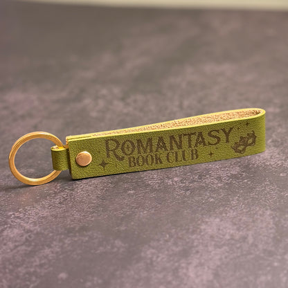 An olive green faux-leather keychain with 'Romantasy book club' etched into it.