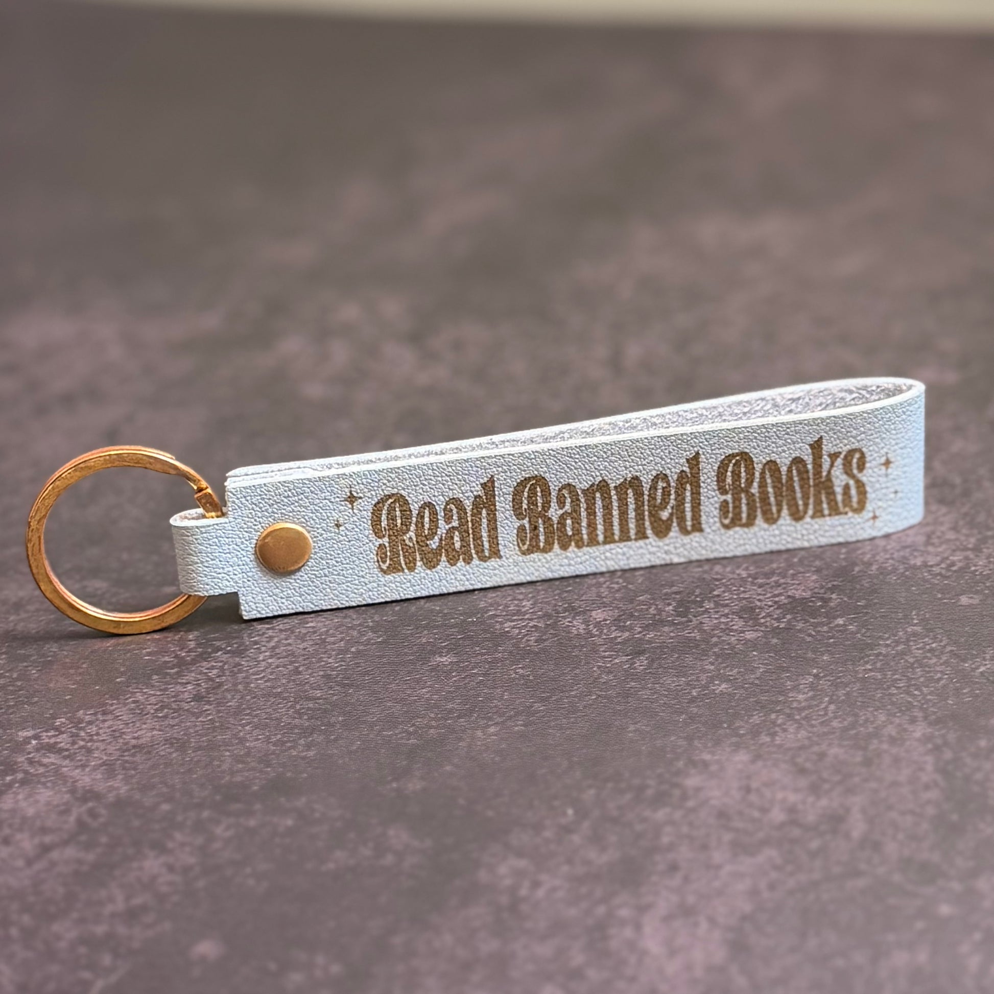 A sky blue faux-leather keychain with 'Read Banned Books' etched into it.