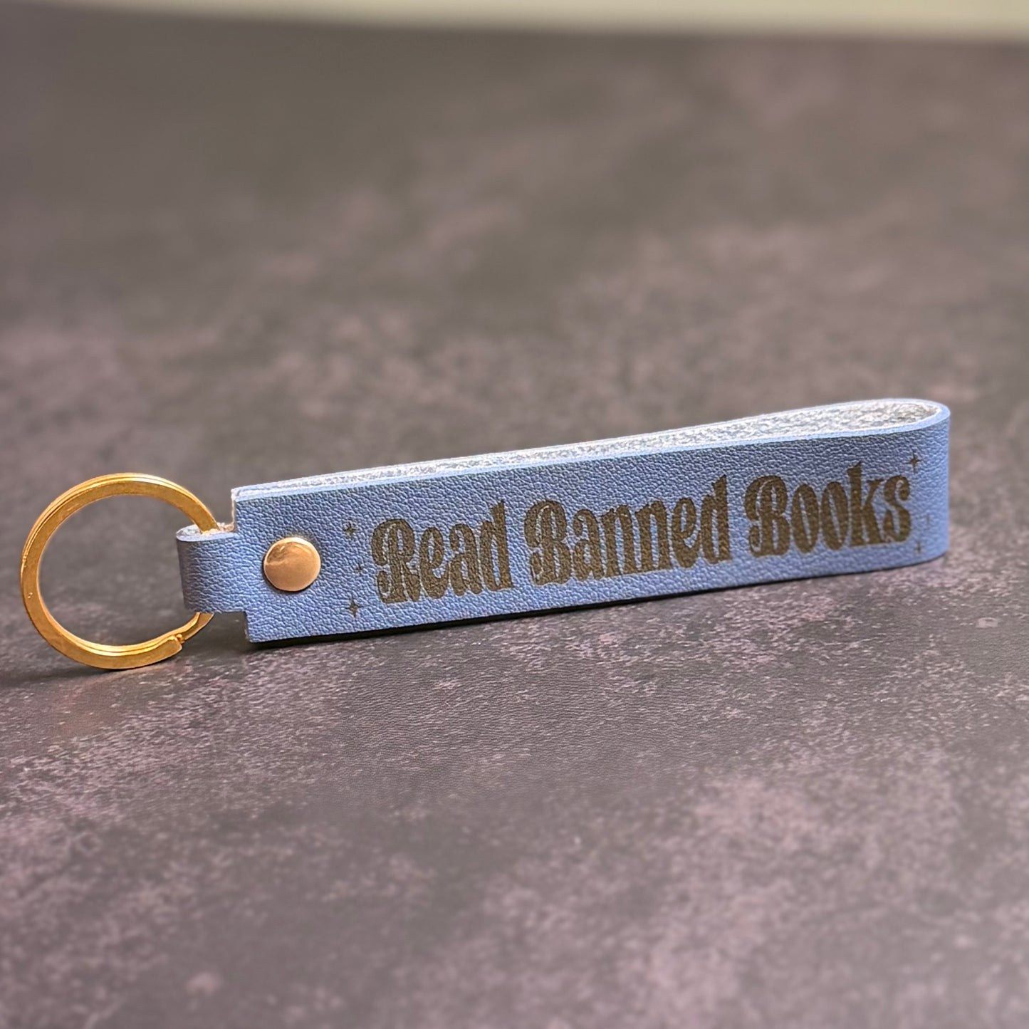 A storm blue faux-leather keychain with 'Read Banned Books' etched into it.