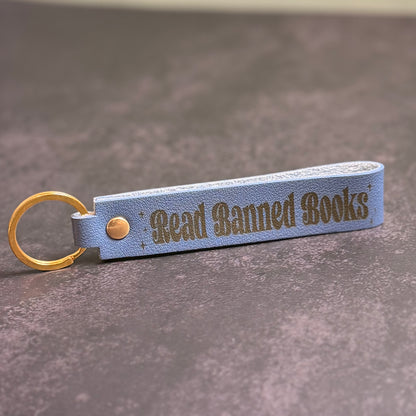 A storm blue faux-leather keychain with 'Read Banned Books' etched into it.