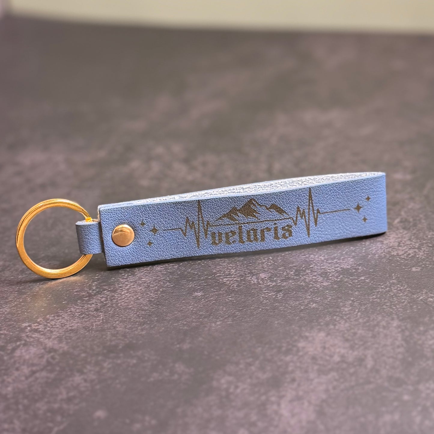 A storm blue faux-leather keychain with 'velaris' etched into it.