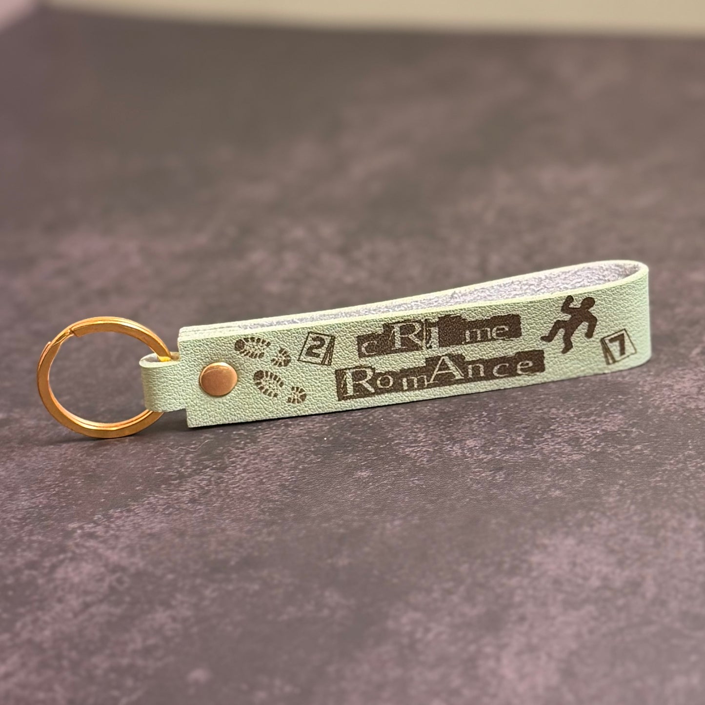 A matcha green faux-leather keychain with 'Crime Romance' etched into it.