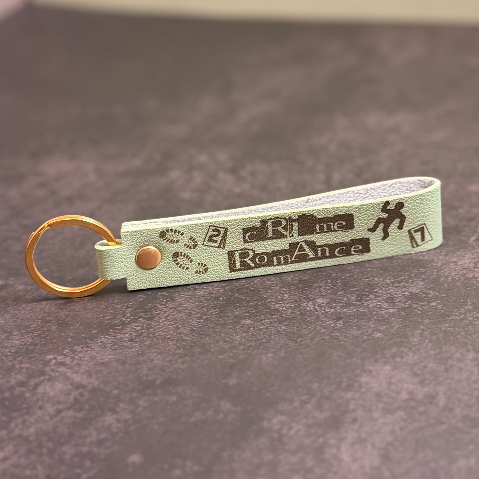 A matcha green faux-leather keychain with 'Crime Romance' etched into it.