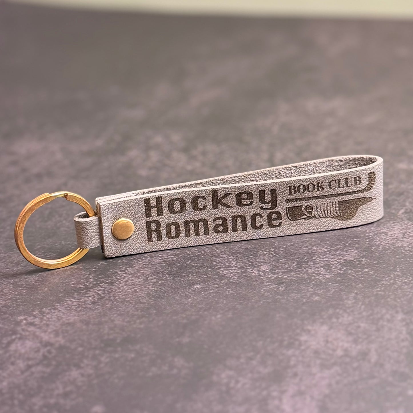 An eggshell white faux-leather keychain with 'Hockey romance book club' etched into it.