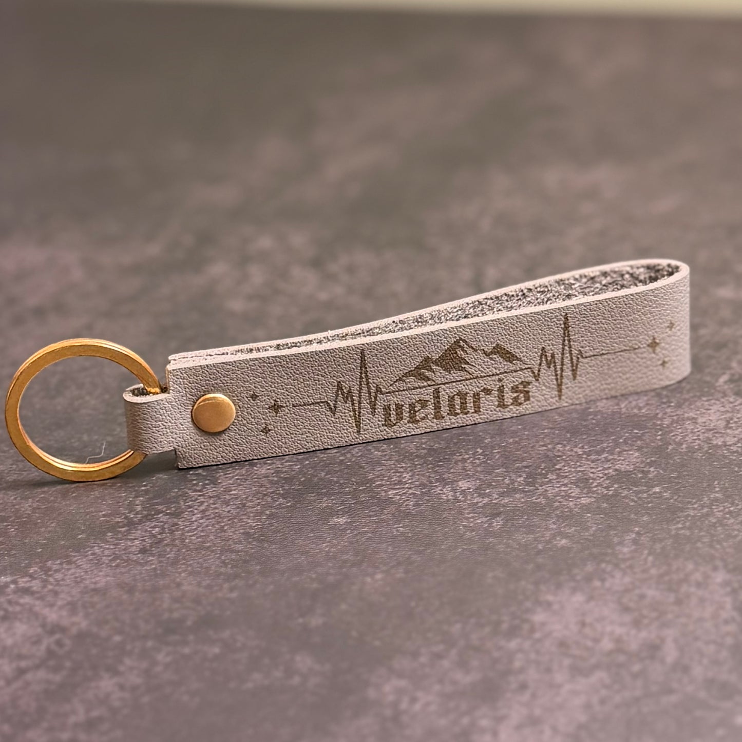 A beige faux-leather keychain with 'velaris' etched into it.