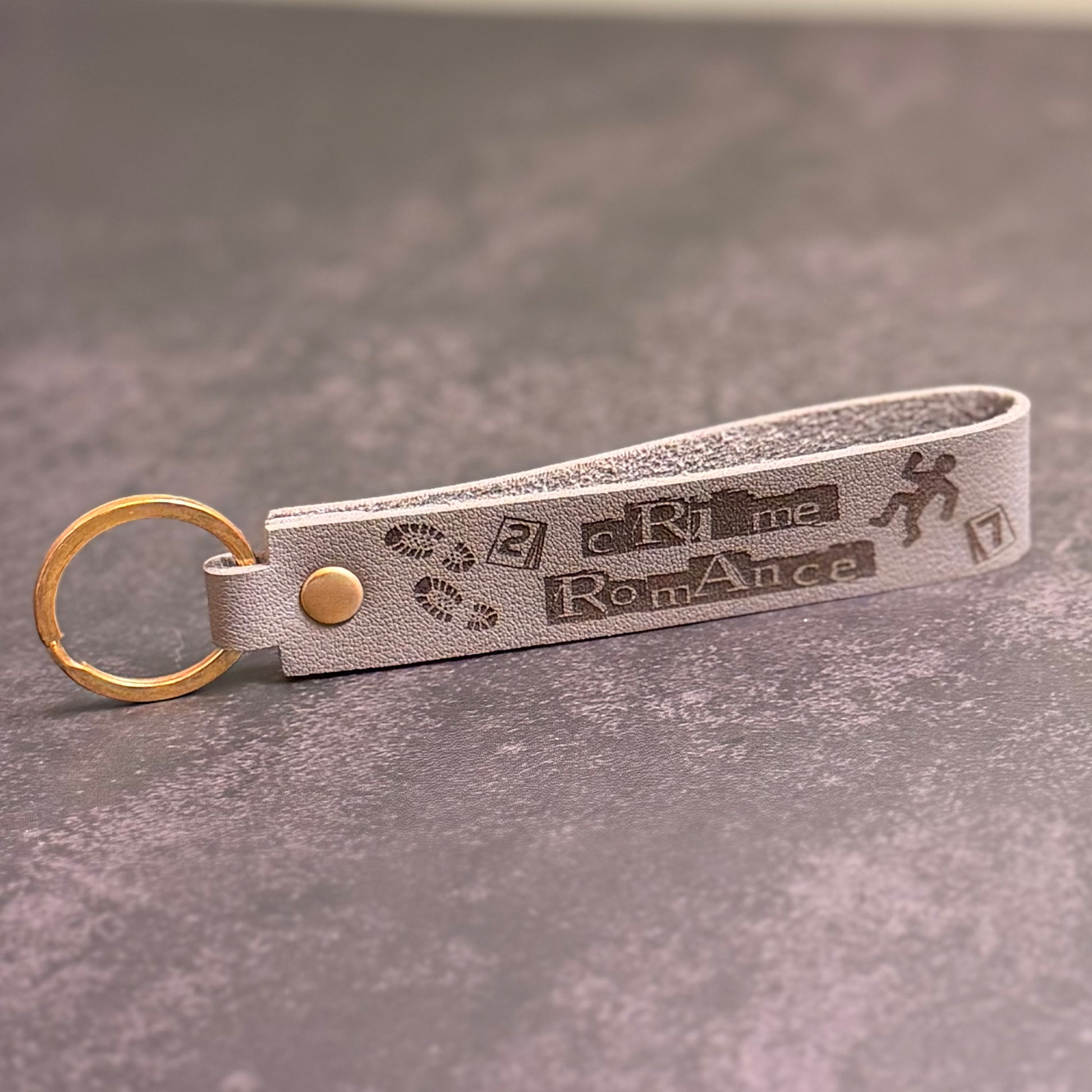 A grey faux-leather keychain with 'Crime Romance' etched into it.