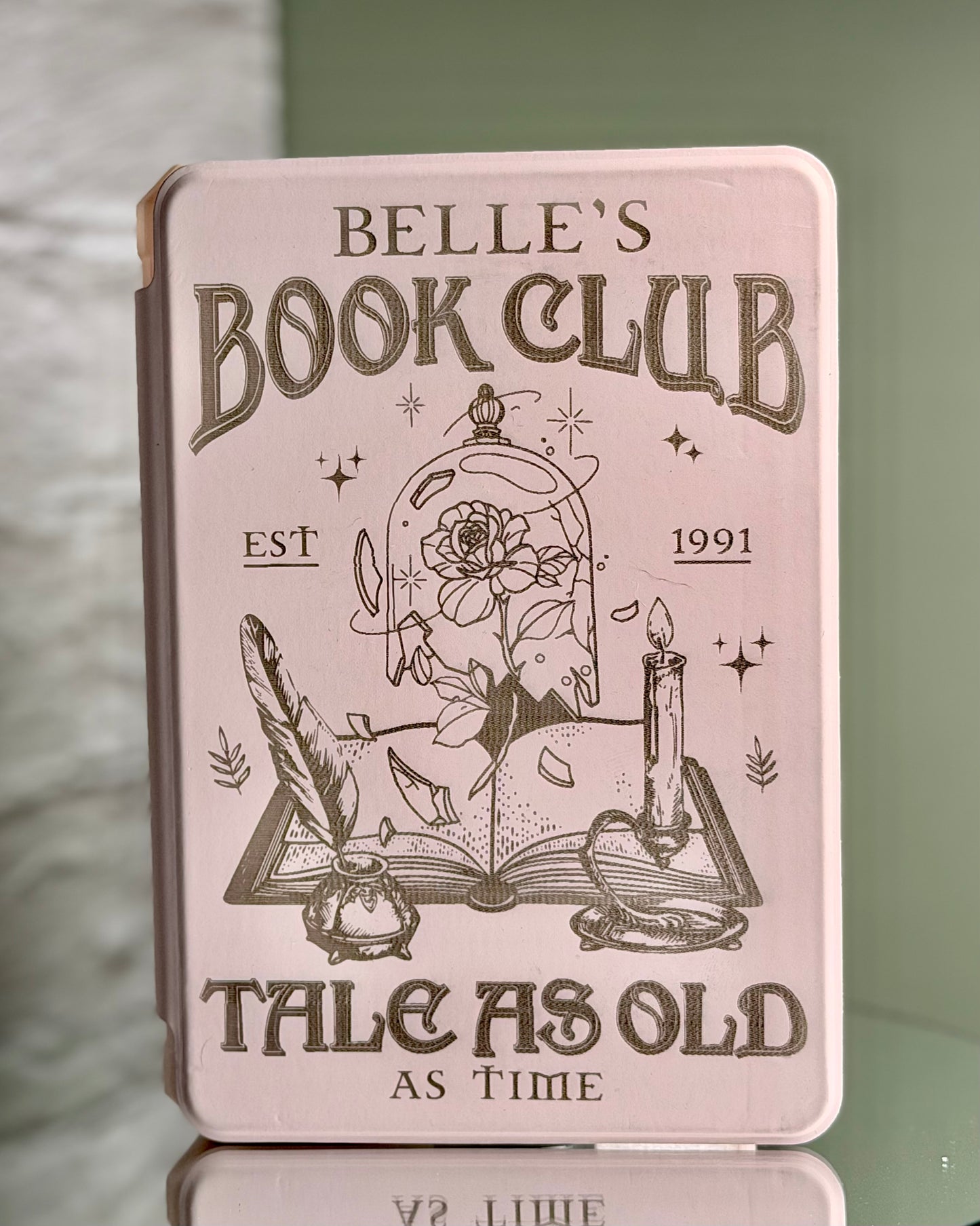 Pink Kindle case with 'Belle's Book Club' design on a reflective surface