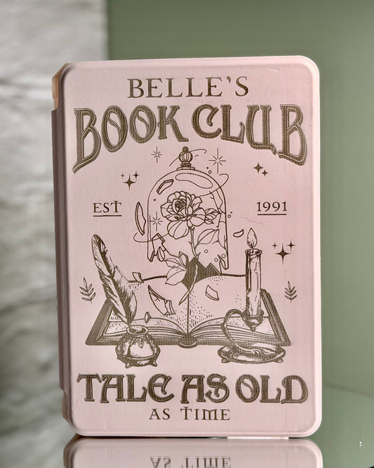 Pink Kindle case with 'Belle's Book Club' design on a reflective surface