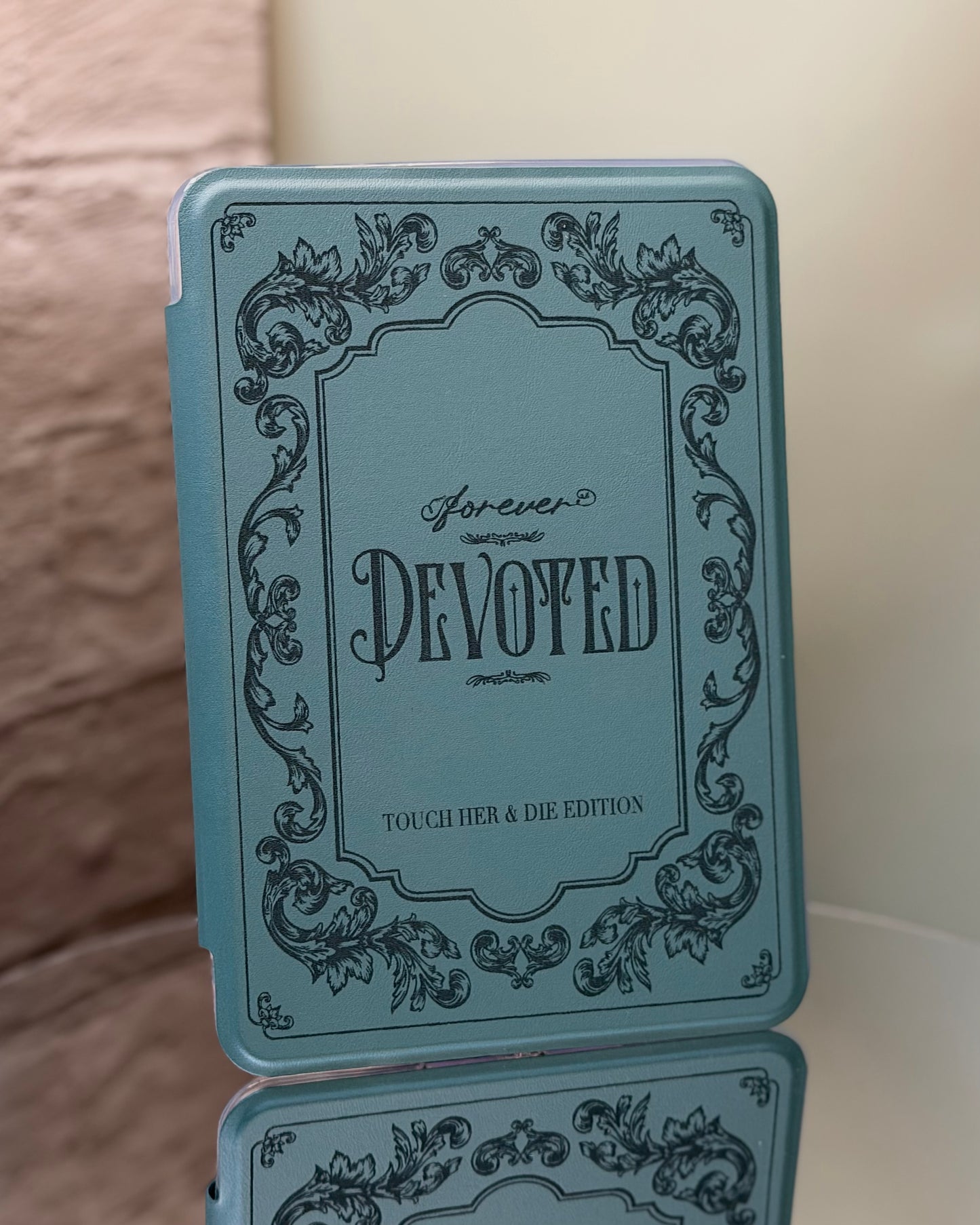 Kindle case with 'Forever Devoted' text and decorative elements on a reflective surface.