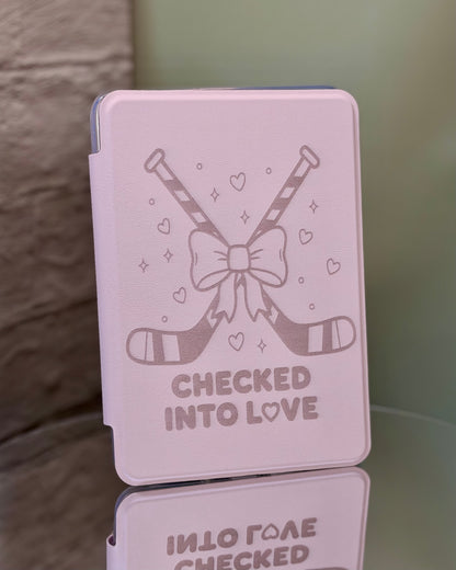 Pink Kindle case with hockey sticks and a bow, featuring the text 'Checked into Love' on a reflective surface. 
