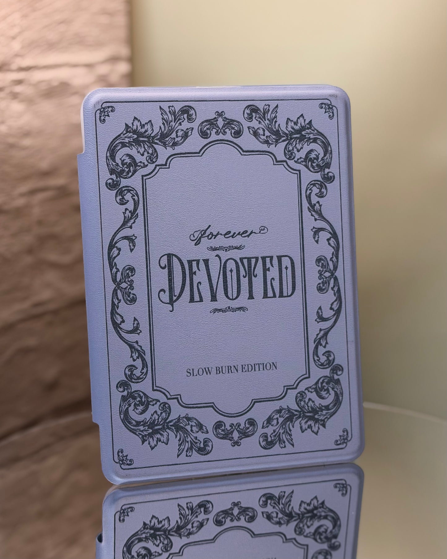 Kindle case with 'Forever Devoted' text and decorative elements on a reflective surface.