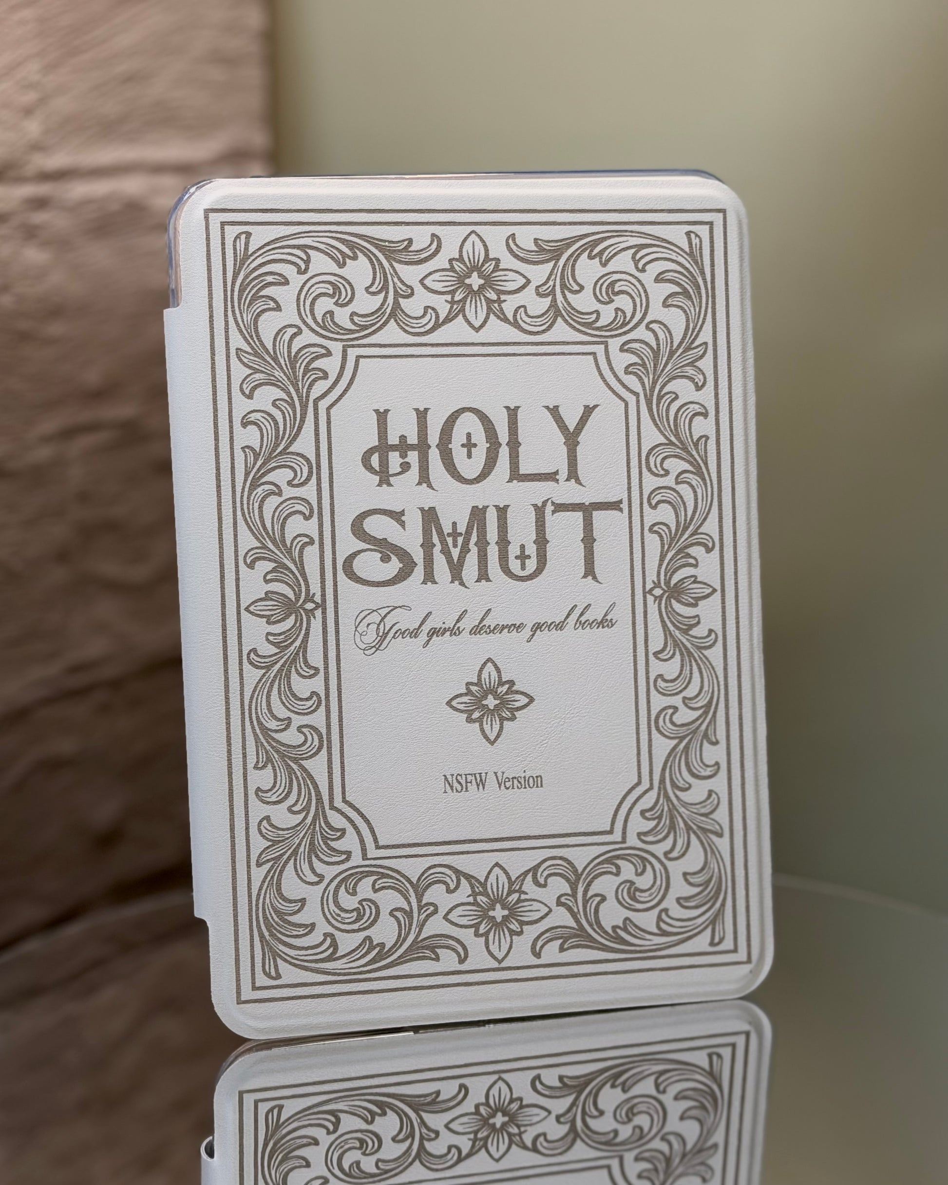 Kindle case with 'Holy Smut' text and decorative border on a reflective surface.