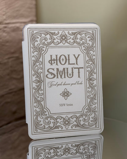 Kindle case with 'Holy Smut' text and decorative border on a reflective surface.