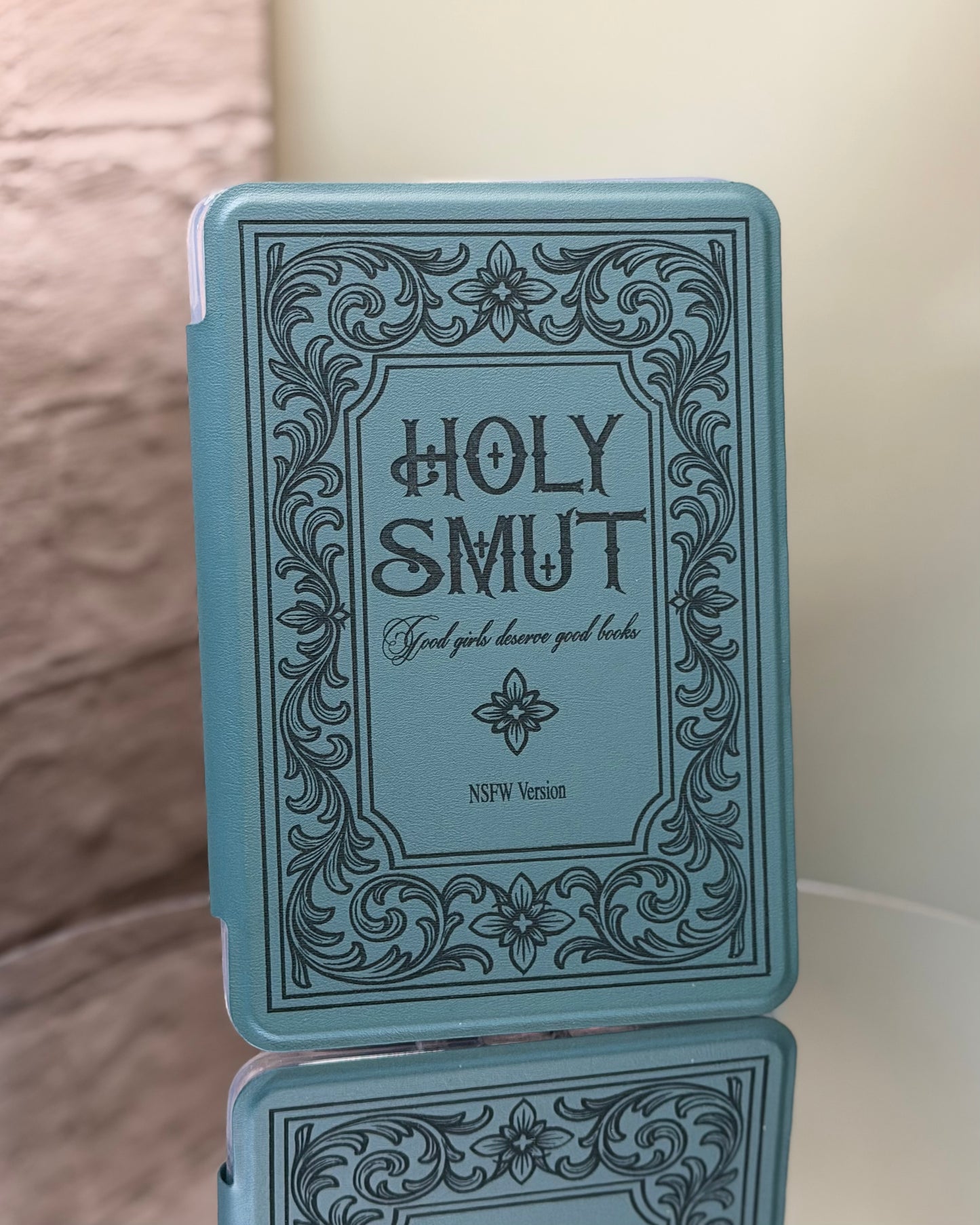 Kindle case with 'Holy Smut' text and decorative border on a reflective surface