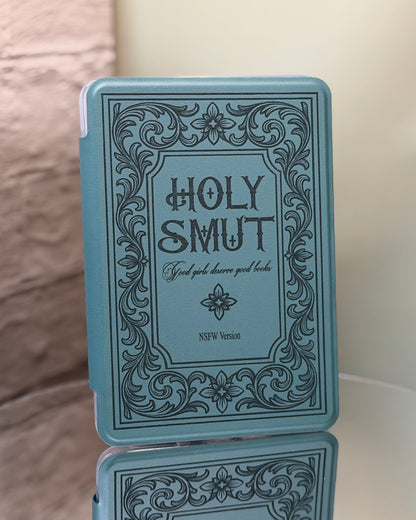 Kindle case with 'Holy Smut' text and decorative border on a reflective surface