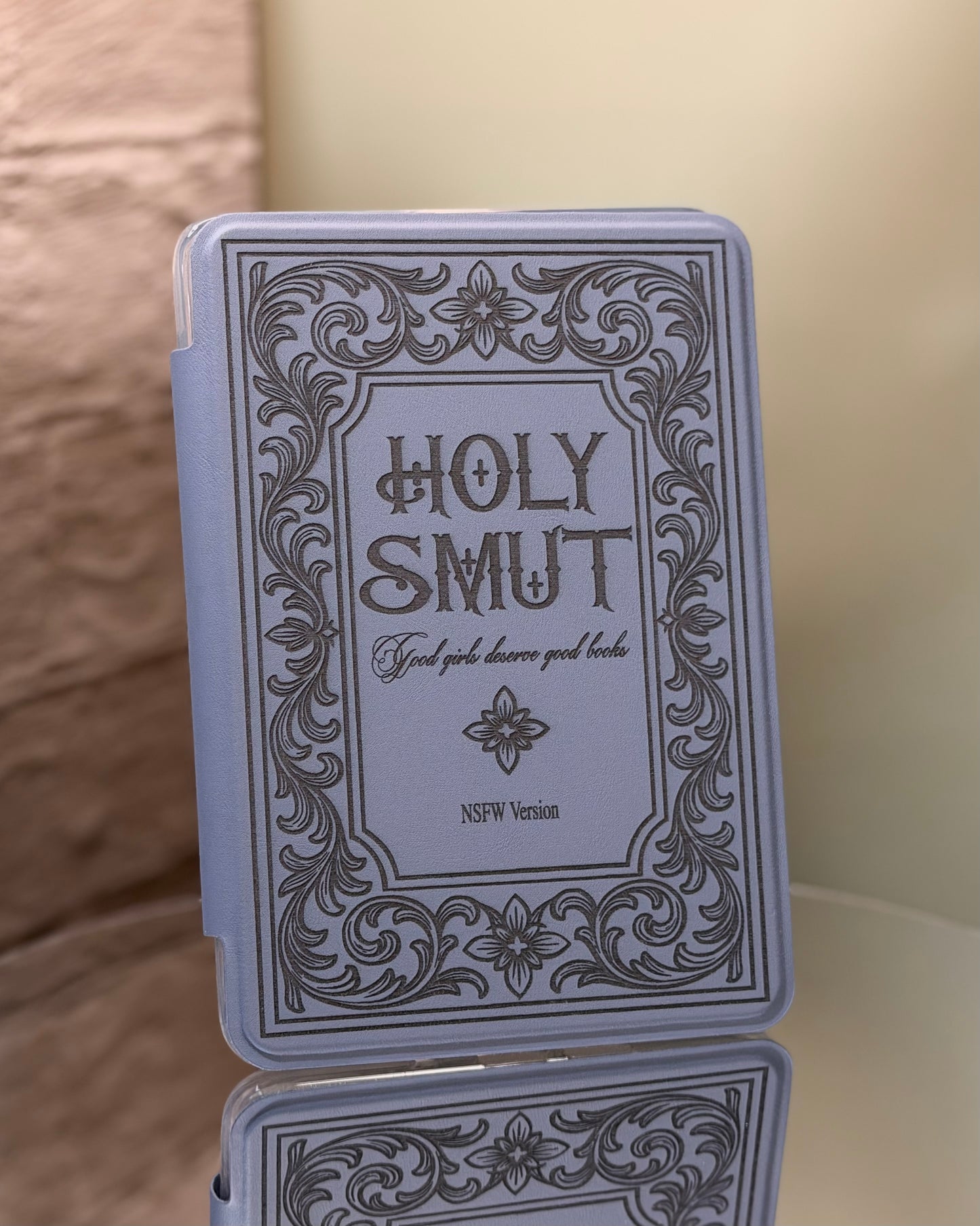 Kindle case with 'Holy Smut' text and decorative border on a reflective 