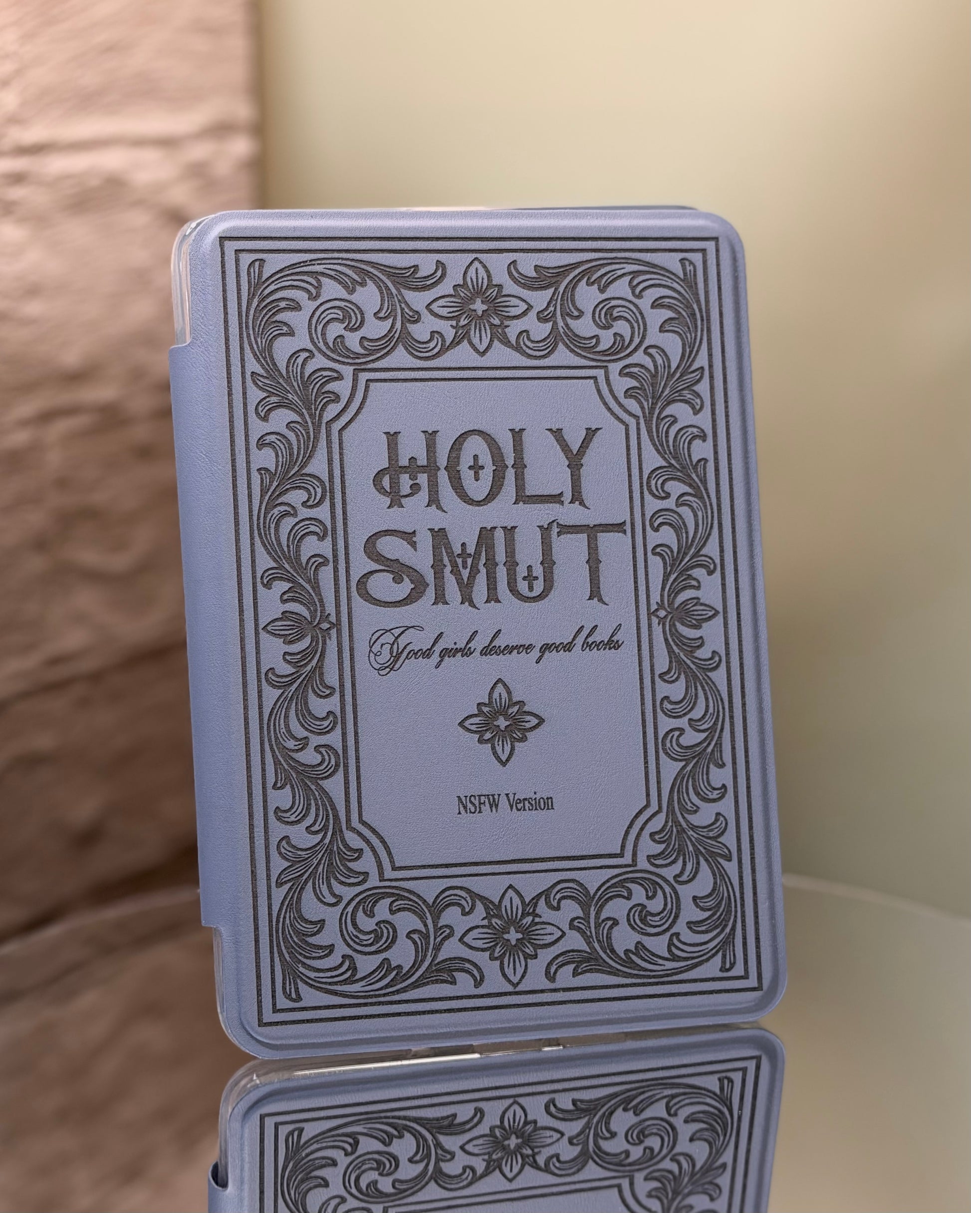 Kindle case with 'Holy Smut' text and decorative border on a reflective 