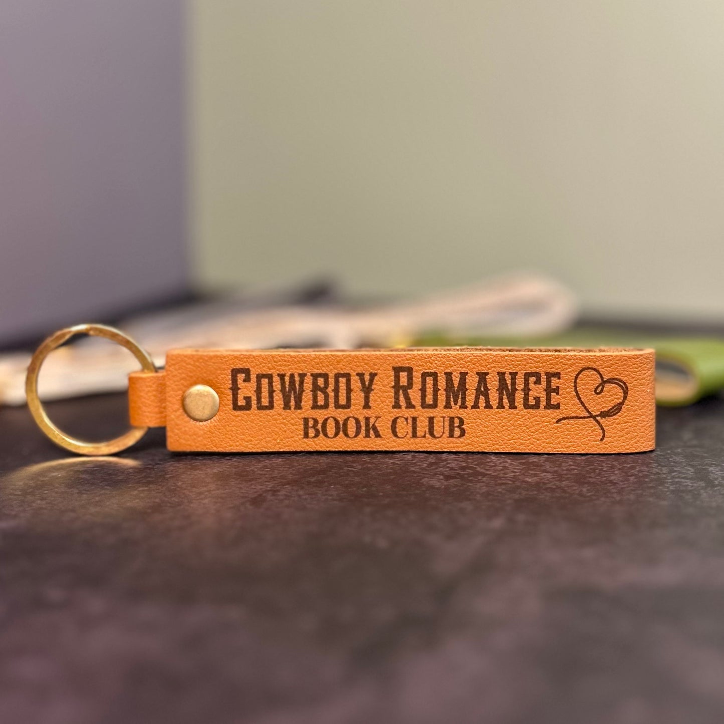A brown faux-leather keychain with 'Cowboy romance book club' etched into it.
