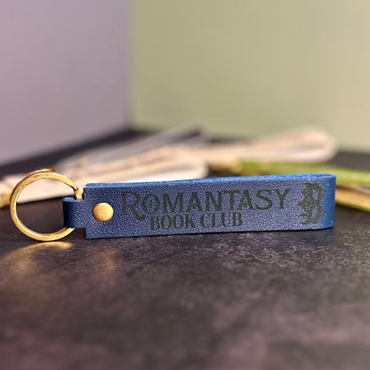 A navy blue faux-leather keychain with 'Romantasy book club' etched into it.
