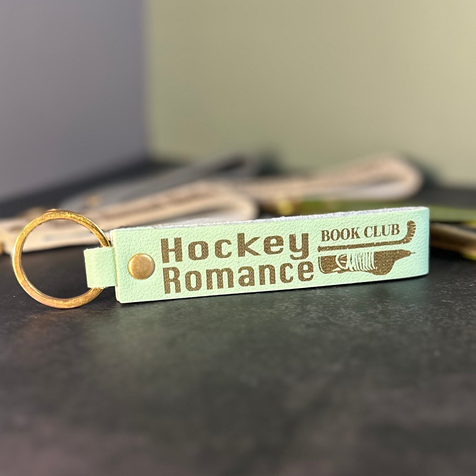 A matcha green faux-leather keychain with 'Hockey romance book club' etched into it.